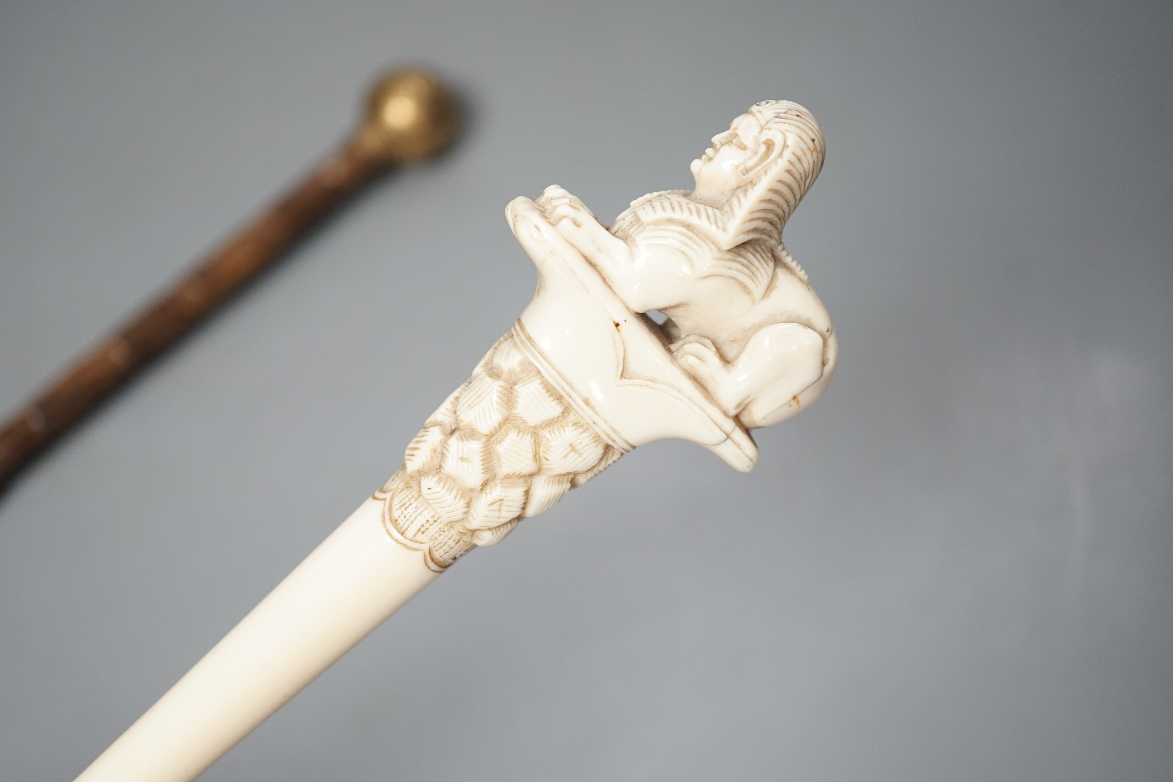 An early 20th century ivory ‘sphinx’ parasol handle, 84cm, together with another gold and iron damascened parasol handle, 62cm